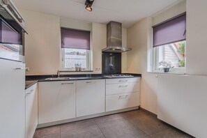 A kitchen with white cabinets, a black countertop, a stainless steel range hood, and a window with a purple blind.
