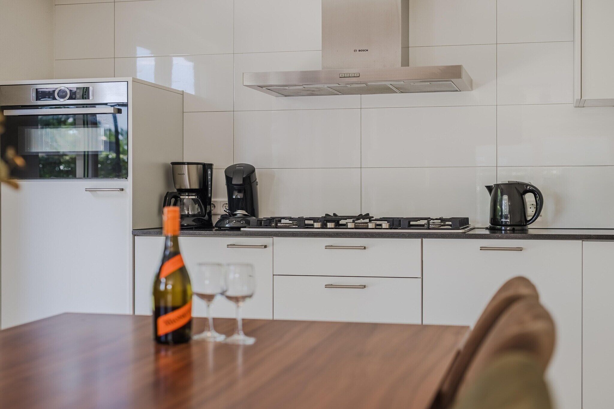 Een moderne keuken met witte kasten, een Bosch oven, een koffiezetapparaat en een waterkoker op het aanrecht.