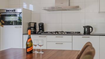 Een moderne keuken met witte kasten, een Bosch oven, een koffiezetapparaat en een waterkoker op het aanrecht.