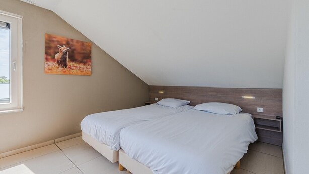 A bedroom with a bed, a nightstand, a wall-mounted light, and a painting. - Villa in Arcen with Private Pool & Wellness (Arcen)