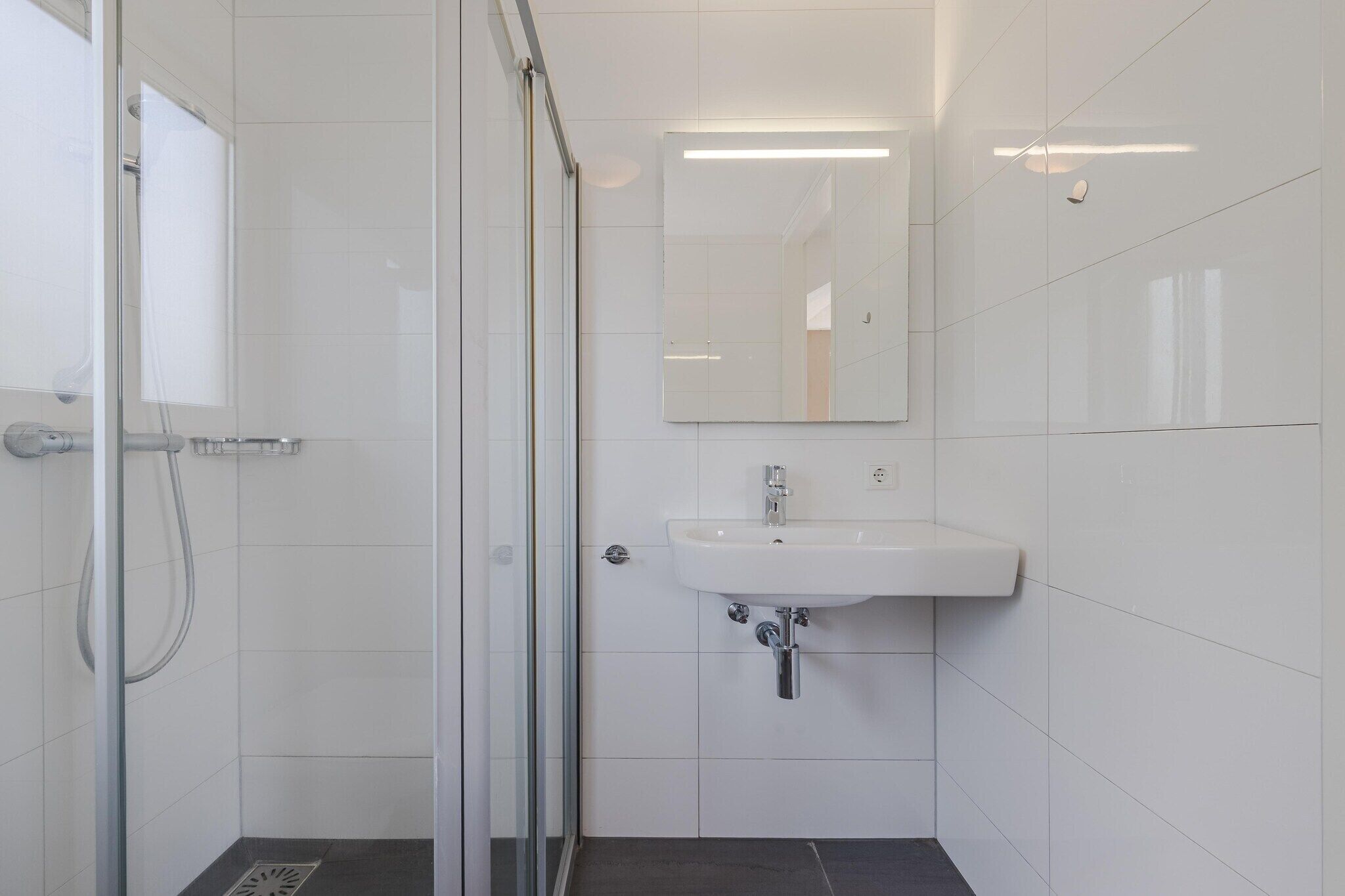 Ein Badezimmer mit Duschkabine aus Glas, einem weißen Waschbecken und einem Spiegel.