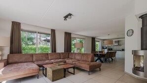 A modern living room with a sectional sofa, a dining table with chairs, and a kitchen area in the background. - Villa in Arcen with Private Pool & Wellness (Arcen)