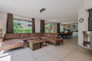 A modern living room with a sectional sofa, a dining table with chairs, and a kitchen area in the background. - Villa in Arcen with Private Pool & Wellness (Arcen)