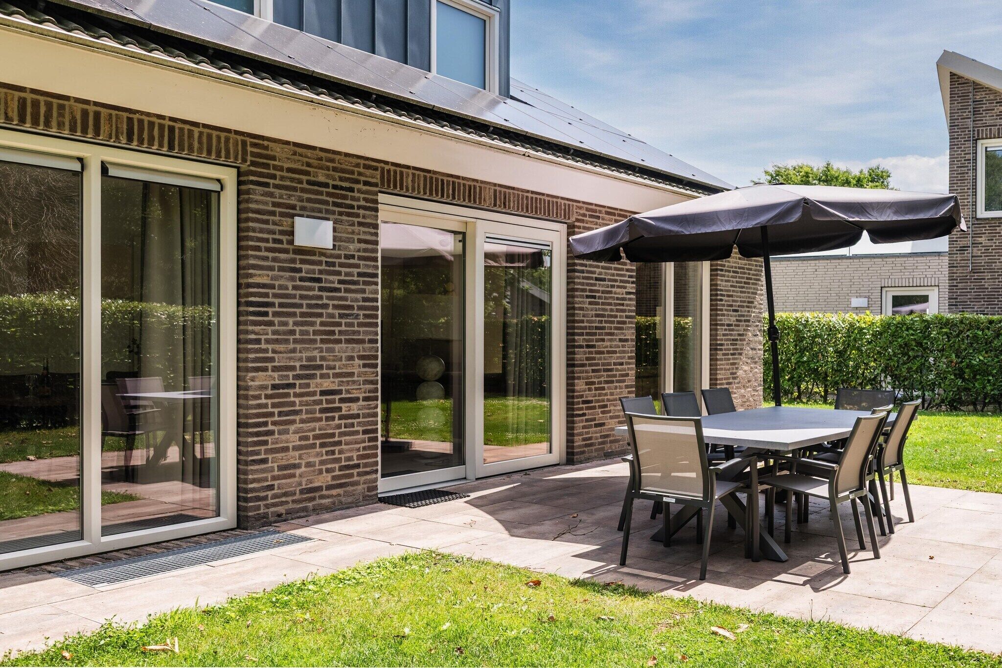 Une terrasse avec une table et des chaises, un parasol et un bâtiment en briques doté de grandes portes vitrées.