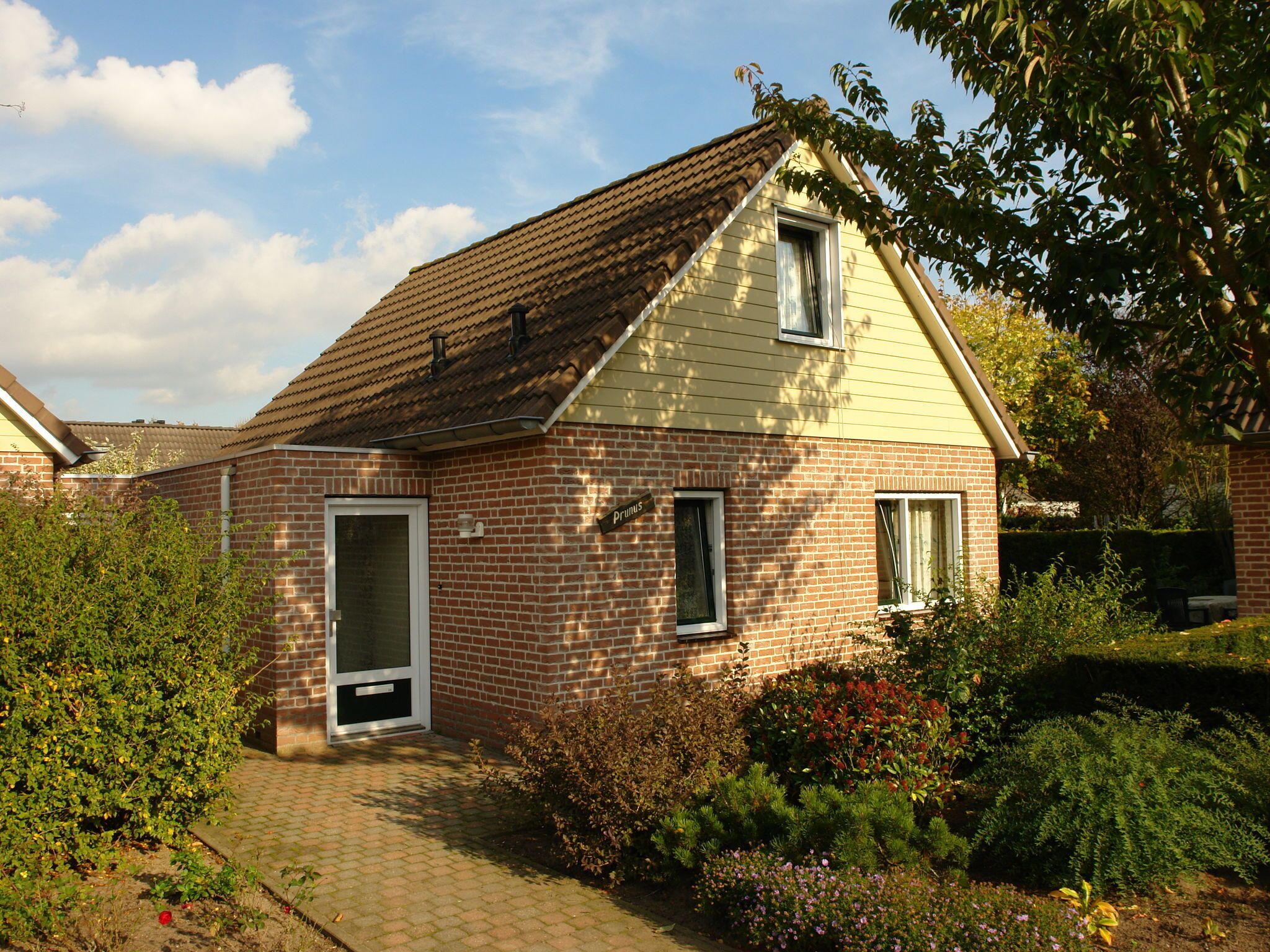 A single-story brick house with a tiled roof, a front door, and a small garden with various plants and flowers.
