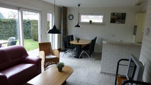 A compact living space with a sofa, a dining table with chairs, a small kitchen area, and a large window offering a view of the outdoors. - Holiday Home in Netherlands with Private Garden (Plasmolen)