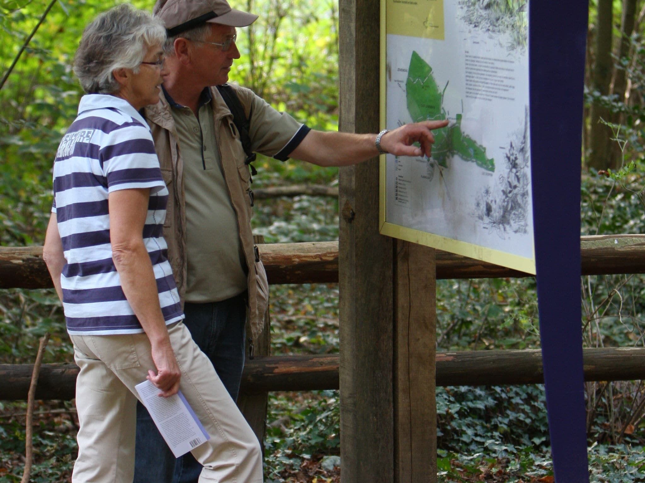 A man and a woman examining a map at a wooden information board in a forested area.