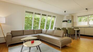 Un salon moderne avec un canapé d’angle, une petite table ronde et un coin repas avec des chaises.