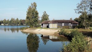 A lakeside building with a thatched roof, a dock, and a sandy beach. - Stylish Woodland Chalet (Hoge Hexel)