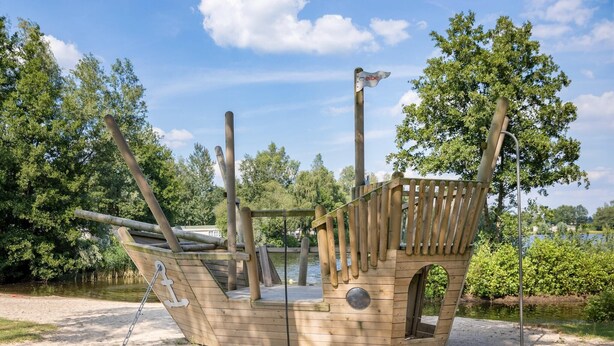 A wooden pirate ship play structure with a ladder, a steering wheel, and a flag. - Stylish Woodland Chalet (Hoge Hexel)