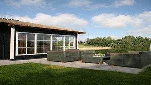 A modern house with large windows, a patio with wicker furniture, and a view of a lake and trees. - Stylish Woodland Chalet (Hoge Hexel)