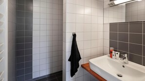 A bathroom with white and dark gray tiles, a white sink with a mirror, and a black towel hanging on the wall. - Chic Stay by the Heathlands (Ruinen)
