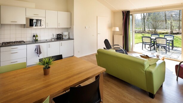 A modern kitchen with white cabinets, a wooden dining table, and a green sofa. - Chic Stay by the Heathlands (Ruinen)