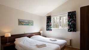 A hotel room with two beds, a painting on the wall, a window with curtains, and a radiator. - Chic Stay by the Heathlands (Ruinen)