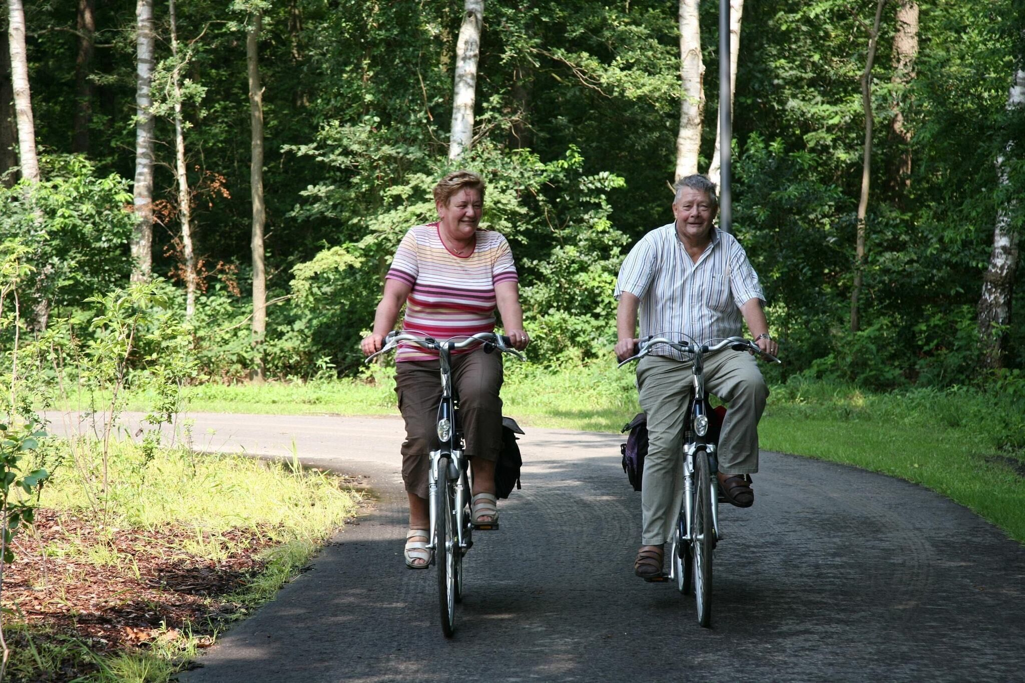 Two people riding bicycles on a paved path surrounded by trees.