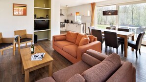 Una sala de estar moderna con un sofá, sillas, una mesa de comedor y una zona de cocina con televisor y electrodomésticos.