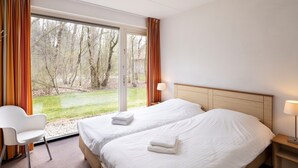 Habitación de hotel con dos camas, una silla, una mesita de noche y vistas a un bosque a través de un ventanal grande.