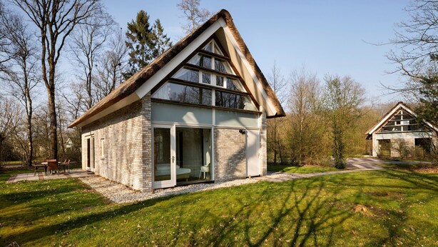 Ein modernes Haus mit geneigtem Dach, großen Glasfenstern und einer Ziegelaußenwand.