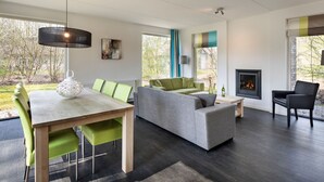 Ein modernes Wohnzimmer mit Esstisch, grünen Stühlen, einem grauen Sofa und einem Kamin.