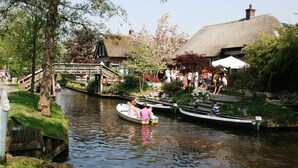 A canal with boats, a wooden bridge, and buildings with thatched roofs. - Lakeside Cottage with Boat (Giethoorn)