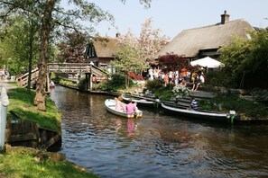Ein Kanal mit Booten, eine Holzbrücke und Gebäude mit strohgedeckten Dächern.