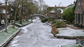 A snow-covered pathway leading to a bridge over a canal, surrounded by residential buildings and greenery. - Lakeside Cottage with Boat (Giethoorn)