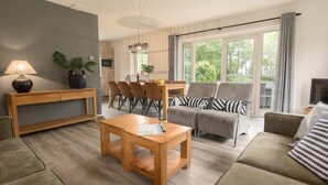A modern living room with a wooden coffee table, grey sofas, and a dining area with chairs and a table. - Thatched Villa in National Park (Paasloo)