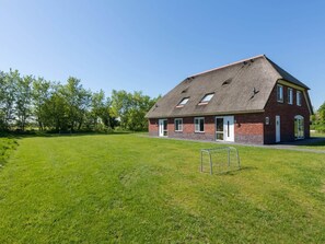 Un bâtiment d’un seul étage, construit en briques, avec un toit en pente, une porte d’entrée et un petit espace clôturé à l’avant.