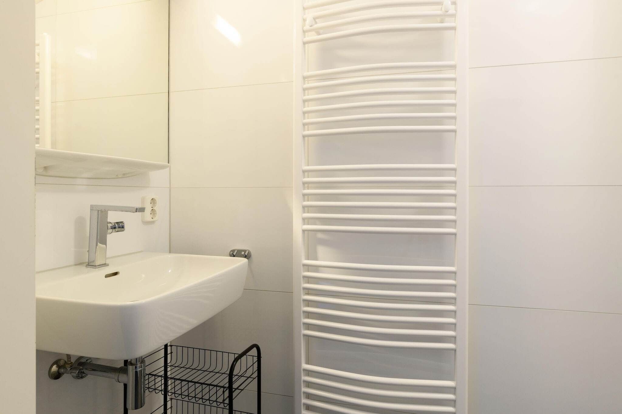 Un baño con lavamanos blanco, espejo y toallero.