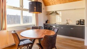 A modern kitchen with a round wooden table and chairs, a large window with curtains, and a unique ceiling design.