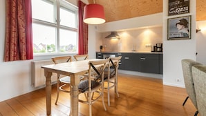 A modern kitchen with a wooden ceiling, a dining table with chairs, and a window with curtains.
