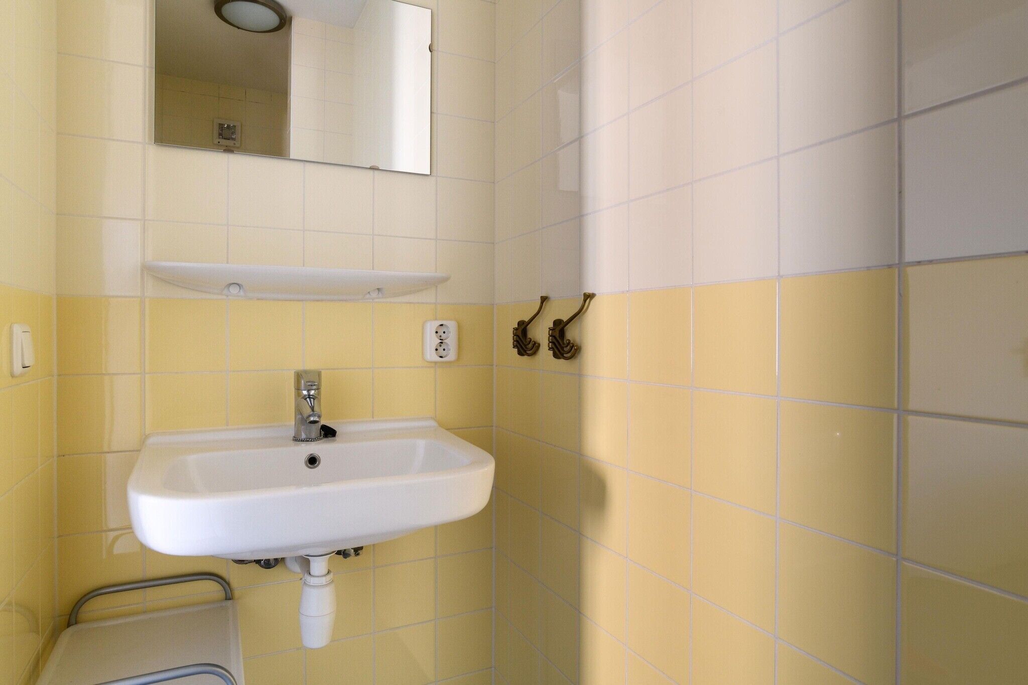 Ein Badezimmer mit Waschbecken in Weiß, gelben Fliesen, einem Spiegel und einem Handtuchhalter.
