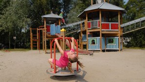 Une aire de jeux avec une structure d’escalade circulaire et une cabane en bois dotée d’un toboggan.