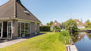 Une maison avec un toit en pente, une entrée avec une porte vitrée et un petit jardin agrémenté d’un bassin.