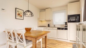 Une cuisine de taille réduite avec des meubles blancs, une table à manger en bois et un luminaire suspendu.