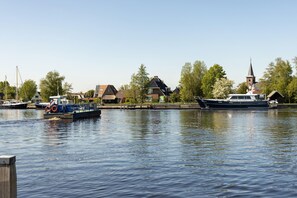 A calm river with boats docked, a church with a steeple, and residential buildings along the shore.