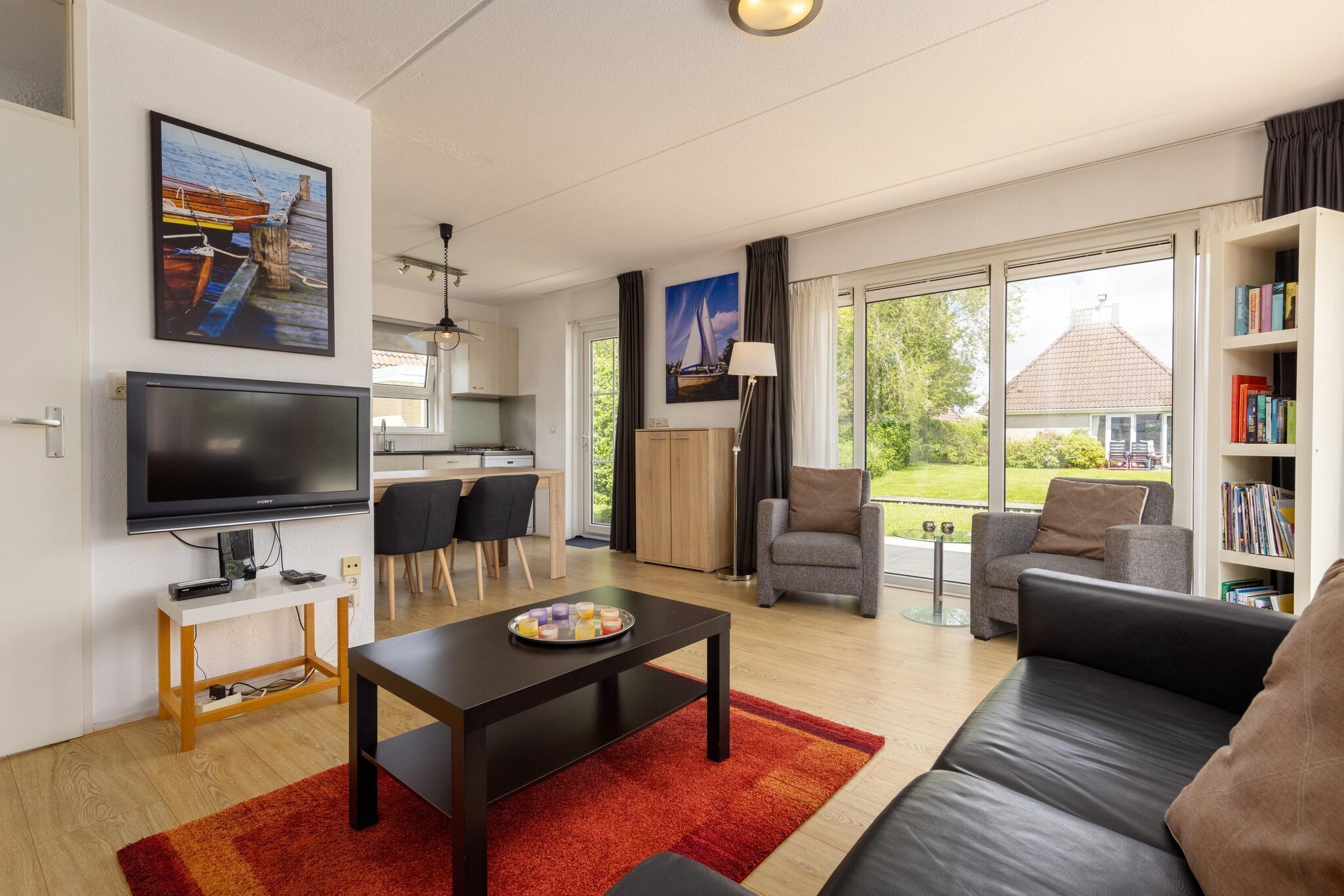 Een moderne woonkamer met een flatscreen televisie, een eethoek met stoelen, een bank en een boekenkast.