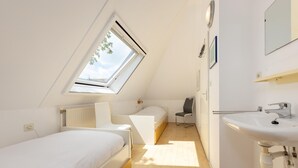 A small, bright room with a skylight, a bed, a chair, and a sink. - Cozy Bungalow with Terrace (Eernewoud)