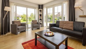 A modern living room with a sofa, armchairs, a coffee table, and a bookshelf. - Cozy Bungalow with Terrace (Eernewoud)