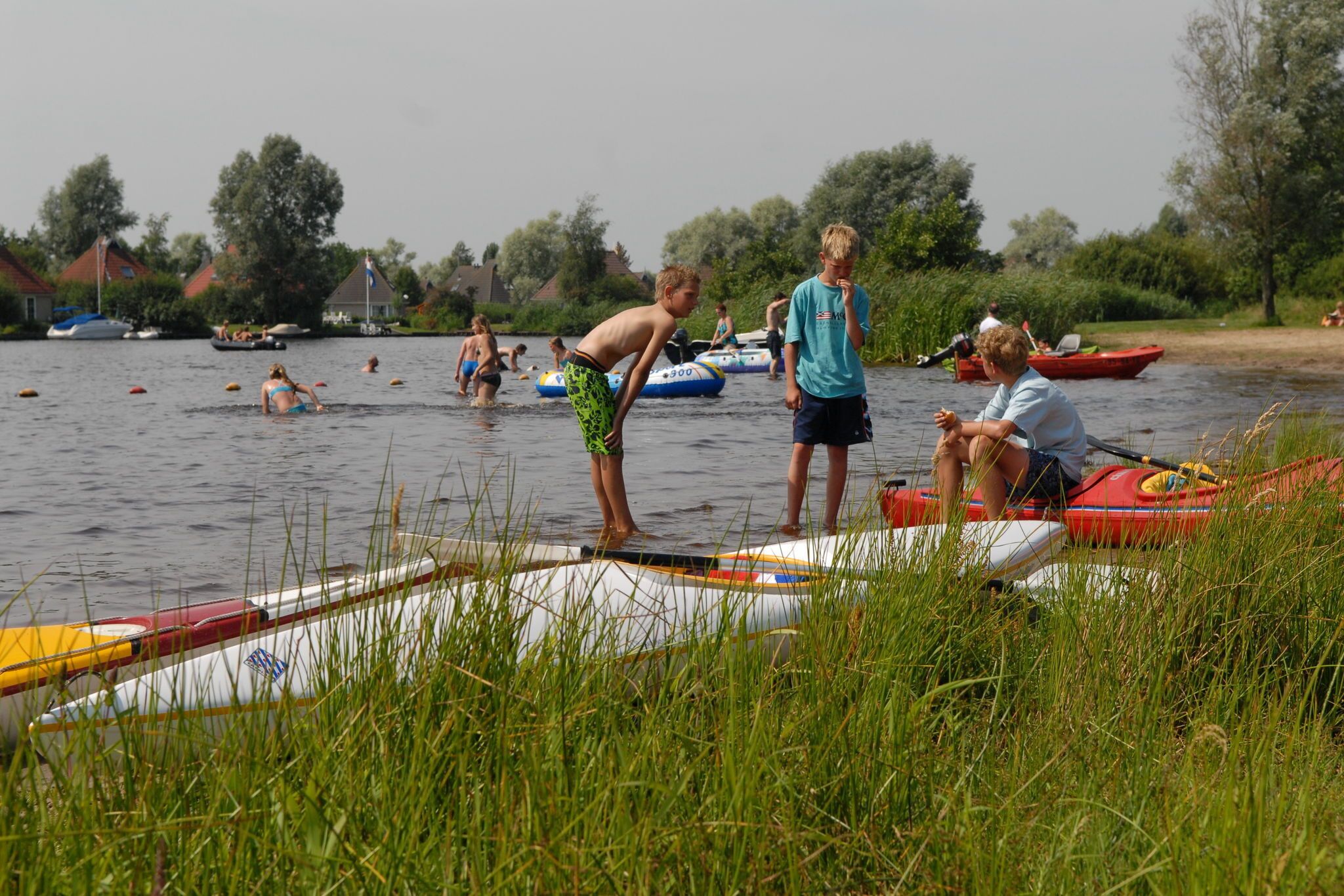 A river with people engaging in water activities, boats, and a grassy bank.