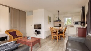 Un espacio habitable compacto con sofá, una mesa de comedor con sillas, televisor, kitchenette y un armario con puerta corredera.
