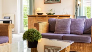 A modern living room with wicker furniture, a glass coffee table, and a view of the outdoors. - Nature Bungalow with Two Baths (Eernewoud)