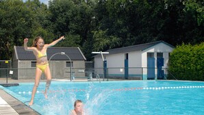 Ein Schwimmbecken mit Sprungbrett, einem Rettungsturm und einem kleinen Gebäude im Hintergrund.