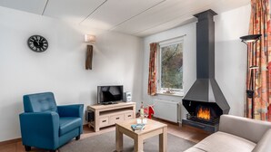 Ein modernes Wohnzimmer mit einer Couch, einem blauen Sessel, einem Holztisch, einem Fernseher und einem Kamin.