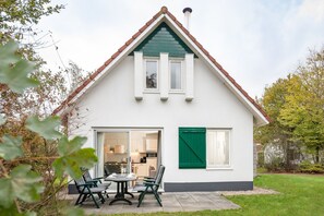 Una casa de dues plantes amb façana blanca, persianes verdes i teulat de rajol.