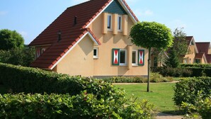A two-story house with a red-tiled roof, beige walls, and a small front garden. - Pet-friendly villa in Park Ankeveen (Tynaarlo)
