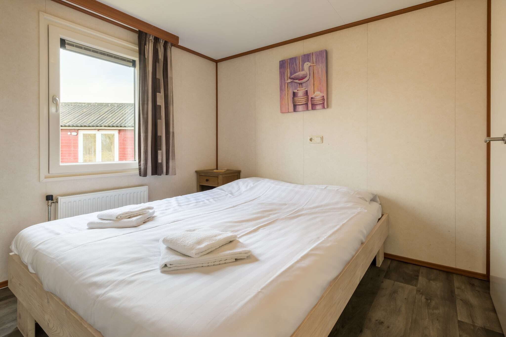 A bedroom with a large bed, a window, a nightstand, and a painting on the wall.