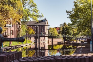Un canal con un puente, un edificio de techo rojo y árboles reflejados en el agua.