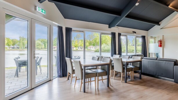 Ett modernt matområde med ett stort bord och stolar, stora fönster med gardiner och utsikt över en innergård.