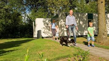 Eine Familie geht mit einem Hund auf einem gepflasterten Weg, im Hintergrund ist ein Gebäude zu sehen.
